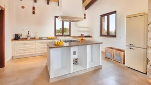 A modern kitchen with white cabinetry, a central island, and a built-in refrigerator. - Country House 'Sant Salvador' with Mountain View, Wi-Fi and Air Conditioning (Illes Balears)