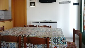 Ein Essbereich mit einem gefliesten Tisch, Stühlen, einem Fernseher und einer kleinen Kommode.