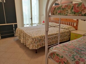 A bunk bed with floral bedding, a wooden headboard, and a small bedside table with drawers.