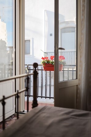 Une chambre avec un lit, une fenêtre et une vue sur un balcon agrémenté de plantes en pot.