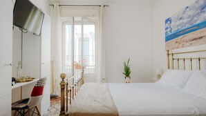 A bedroom with a bed, a desk with a chair, a TV mounted on the wall, and a window with curtains. - Room 'Lunedì' with Balcony, Wi-Fi and Air Conditioning (Carovigno)