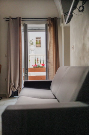 Une pièce avec un canapé, une fenêtre avec des rideaux, un mur blanc et un balcon agrémenté de plantes en pot.