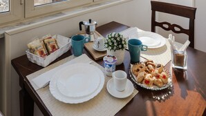 A dining table with plates, cups, and pastries, set against a window with a view of buildings.