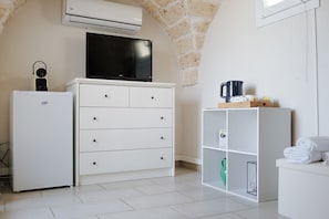Une pièce comprenant une commode blanche, un meuble blanc, un téléviseur à écran plat, une machine à café et un vase vert.