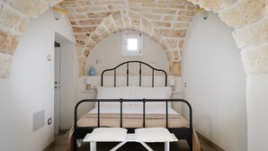 A narrow room with a stone arch ceiling, a bed with a metal frame, a small window, and a bedside table with a lamp. - Room 'Serranova' with Private Terrace, Wi-Fi and Air Conditioning (Carovigno)