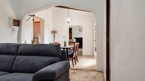 A living room with a sofa, a dining area with a table and chairs, and a kitchen visible through an archway.