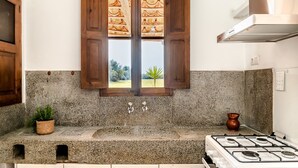 A kitchen with a granite countertop, a gas stove, a window with wooden shutters, and a potted plant.