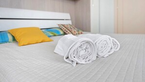 A neatly made bed with a rolled white towel, a yellow pillow, and a patterned pillow on a quilted bedspread. - Room 'Swan Matrimoniale Green' with Shared Pool, Wi-Fi and Air Conditioning (Manerba del Garda)