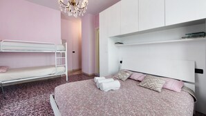 Une chambre avec des lits superposés, un grand lit avec des serviettes roulées, un lustre et des rangements intégrés blancs.