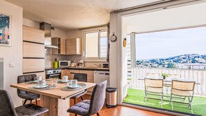 A modern kitchen with wooden cabinets, a dining area with a table and chairs, and a balcony with a view of a town.