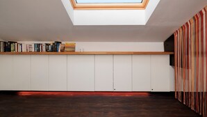 A room with a skylight, a bookshelf, a wooden floor, and a striped curtain.