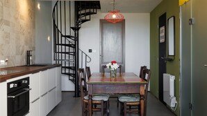 A modern kitchen with a spiral staircase, a dining table with chairs, and a red pendant light.