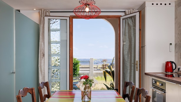 A dining area with a table, chairs, a vase with flowers, and a view through an open door.