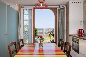 Un comedor con una mesa, sillas, un florero con flores y vistas a través de un umbral abierto.