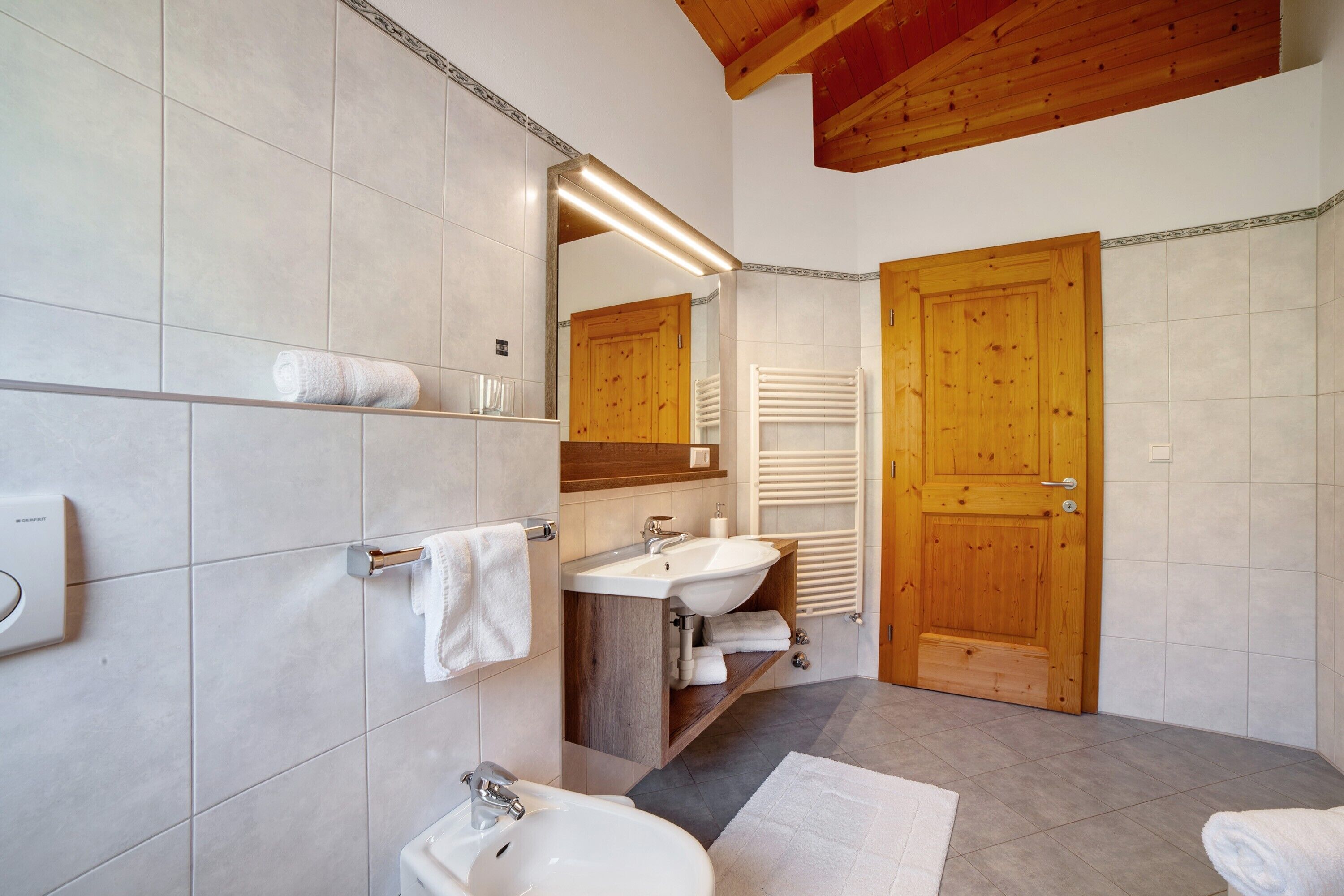 Ein Badezimmer mit Holztür, Waschbecken, Spiegel und Handtuchhalter.