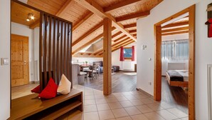 A spacious room with a high ceiling, wooden beams, a bench with cushions, a dining area, and a bed.