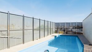 An outdoor swimming pool with a metal ladder, surrounded by a fence with a grid pattern. - Apartment 'Sevilla Centro Con Piscina' with Shared Pool, Wi-Fi and Air Conditioning (Sevilla)
