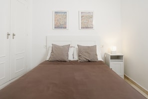 Ein Schlafzimmer mit einem Bett, zwei Kissen, einem Nachttisch, einer Lampe und zwei gerahmten Bildern an der Wand.