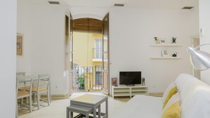 A living room with a sofa, a TV on a stand, a small table, and chairs. - Apartment 'Sevilla Centro Con Piscina' with Shared Pool, Wi-Fi and Air Conditioning (Sevilla)