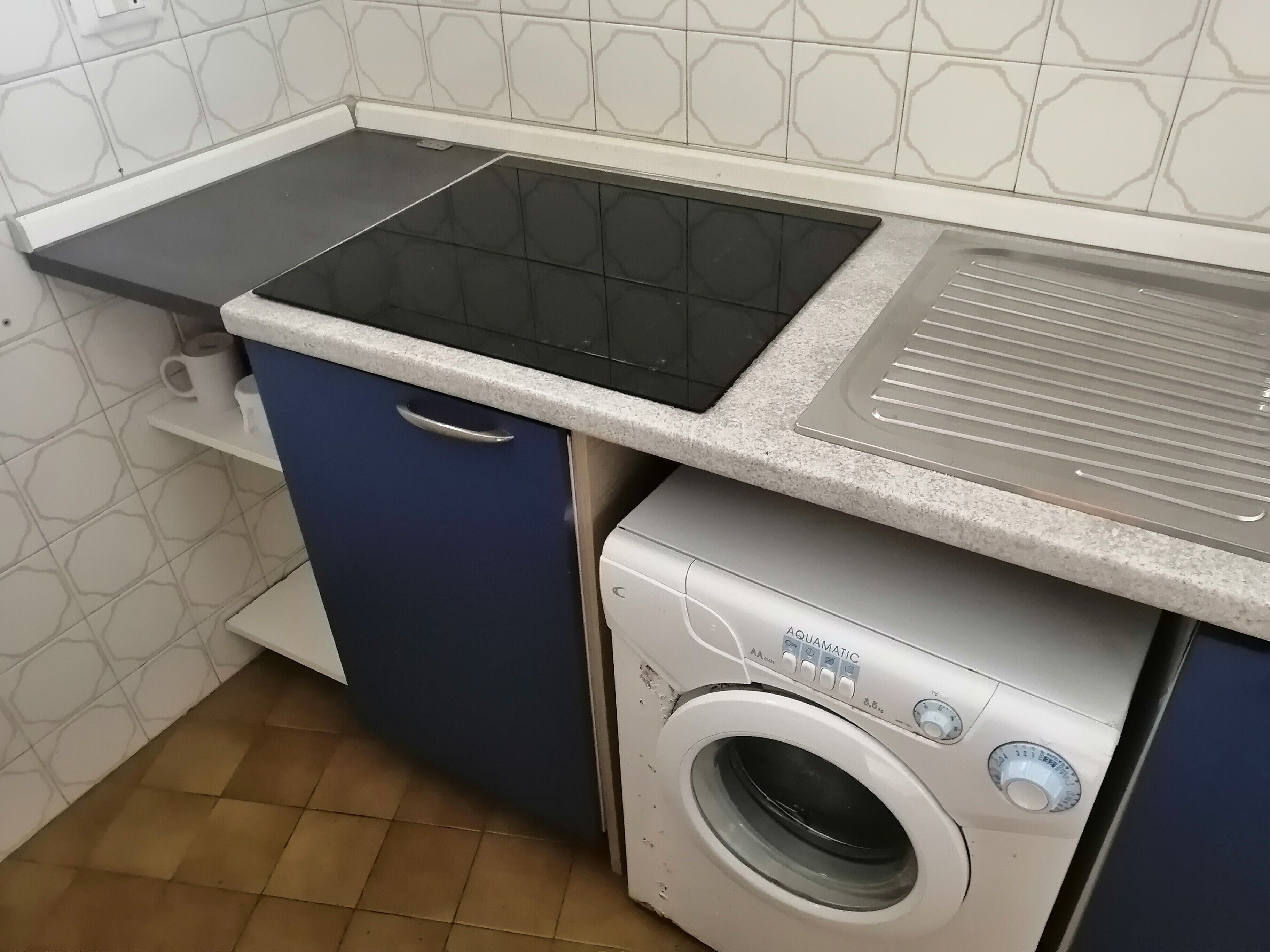Une cuisine dotée d’une plaque de cuisson à induction noire, d’un four encastré, d’un évier en acier inoxydable et d’un lave-linge à chargement frontal.