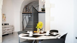 Un coin repas avec une table ronde, des chaises, un vase rempli de fleurs jaunes, une machine à café et un escalier en arrière-plan.