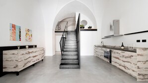 Une cuisine moderne avec un escalier central, des murs blancs et un décor minimaliste.