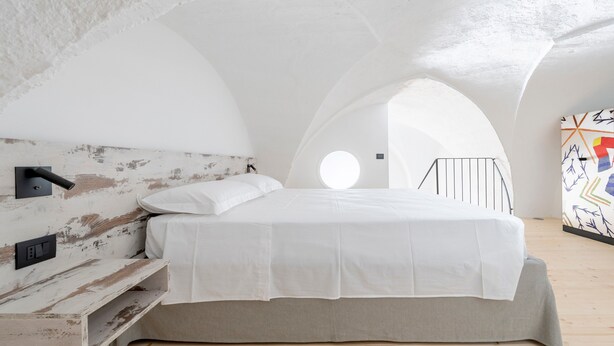 Une chambre aménagée dans les combles, avec un lit, une lampe fixée au mur et une lucarne circulaire.