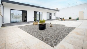 Un edificio moderno con amplios ventanales, techo plano y patio de grava con plantas en macetas.