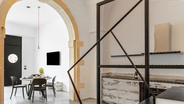 Un interior moderno con comedor, pantalla de marco negro y una escalera.