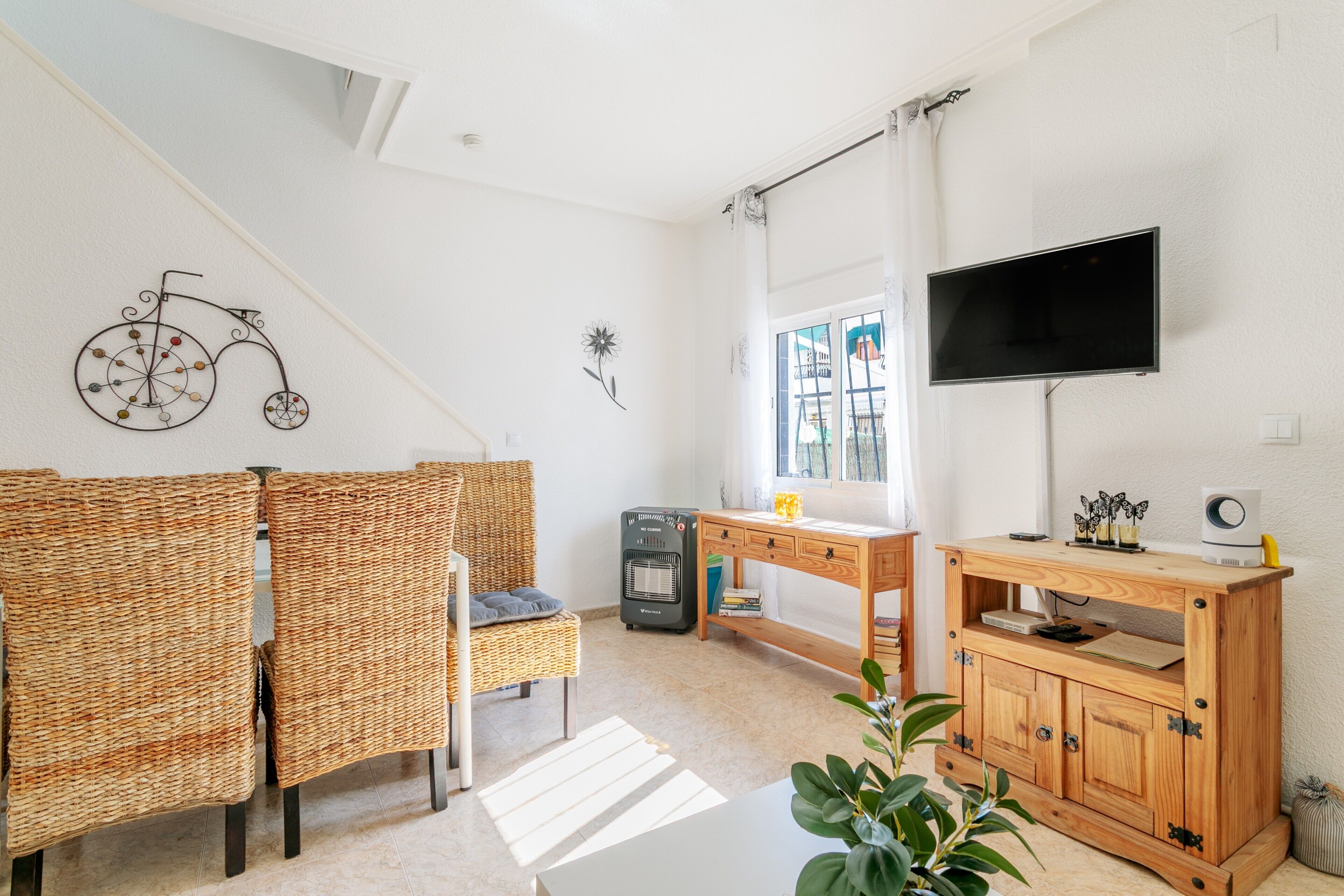 Een kamer met rieten stoelen, een houten bureau, een televisie en een raam met gordijnen.