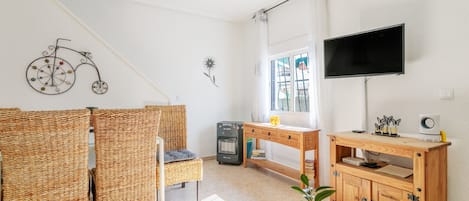 A room with wicker chairs, a wooden desk, a television, and a window with curtains.