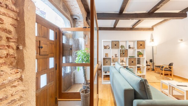 Ein Zimmer mit Holztür, Fenster, Bücherregal, Sofa und Lampe.