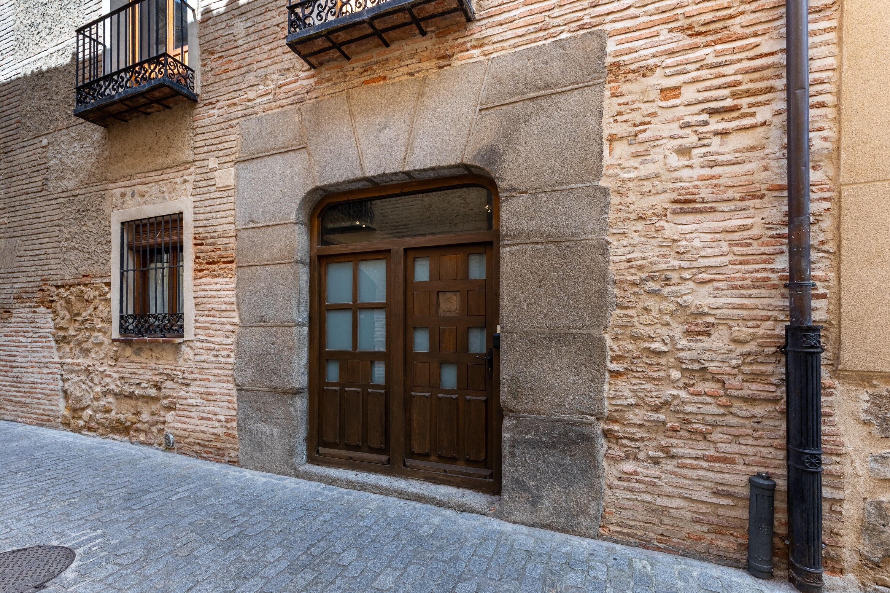 A stone building with a wooden door, a window with metal bars, and a black metal railing on the upper floor.