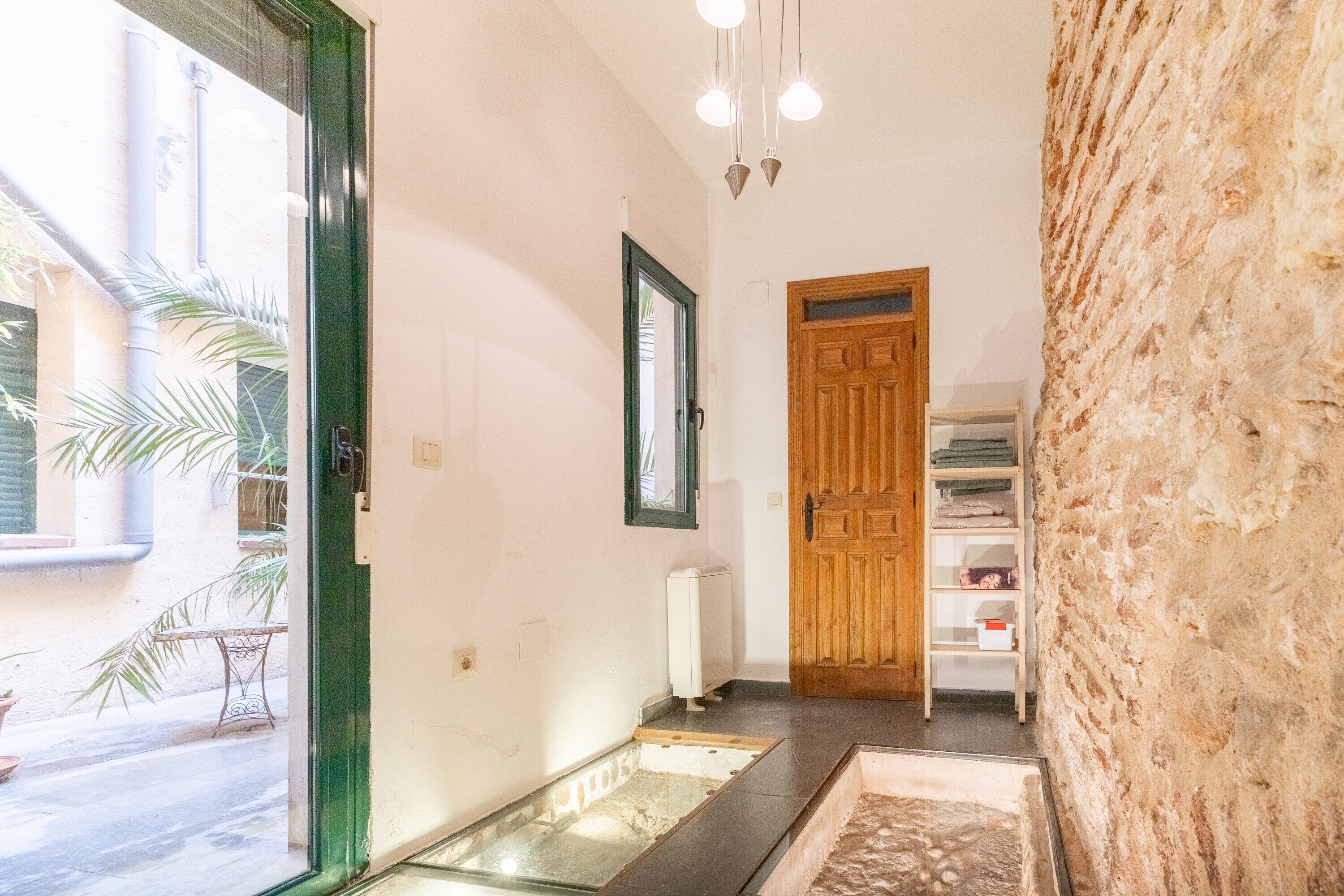 A hallway with a wooden door, a radiator, a small table, and a shelf with items.