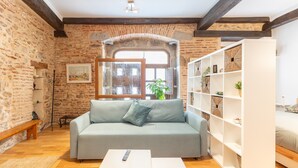 Ein Zimmer mit Steinwand, einer Holzbank, einem grauen Sofa, einem weißen Bücherregal und einem Fenster mit Aussicht.