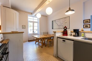 A kitchen with a wooden table, chairs, a map on the wall, a coffee maker, and a dishwasher.