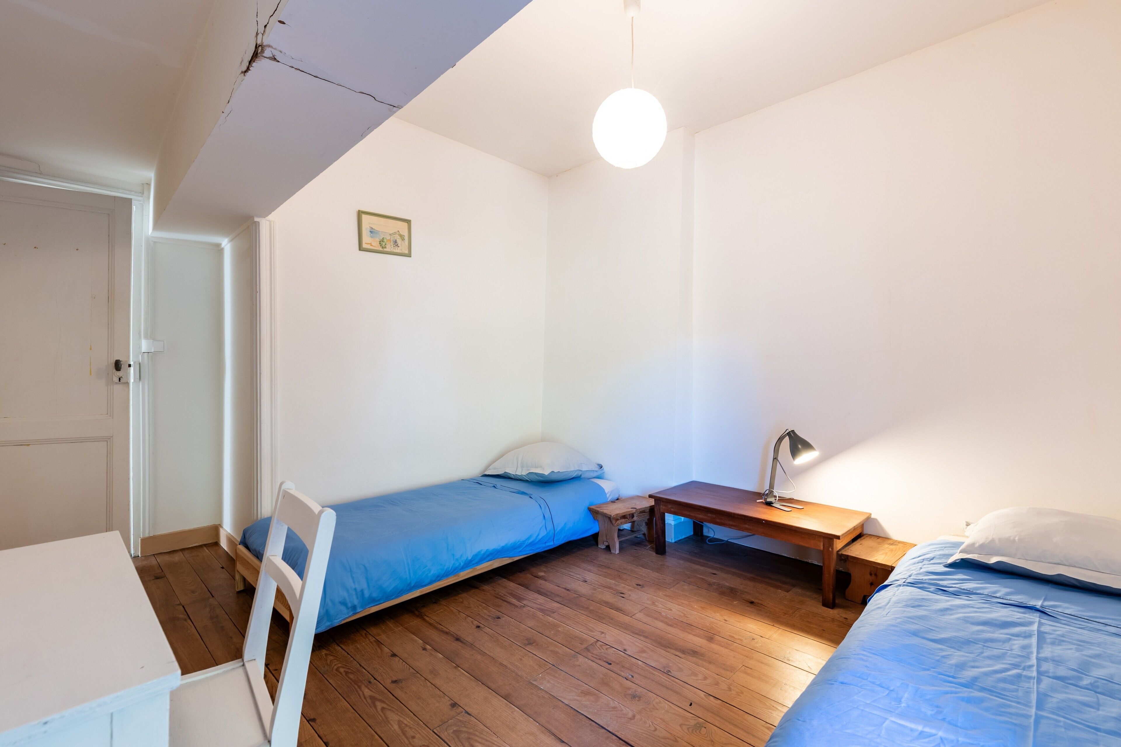 A small room with a bed, a desk, a chair, and a wooden floor.