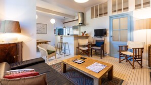 A modern living room with a sofa, coffee table, and chairs, a kitchen area with cabinets and a stove, and a blue door.