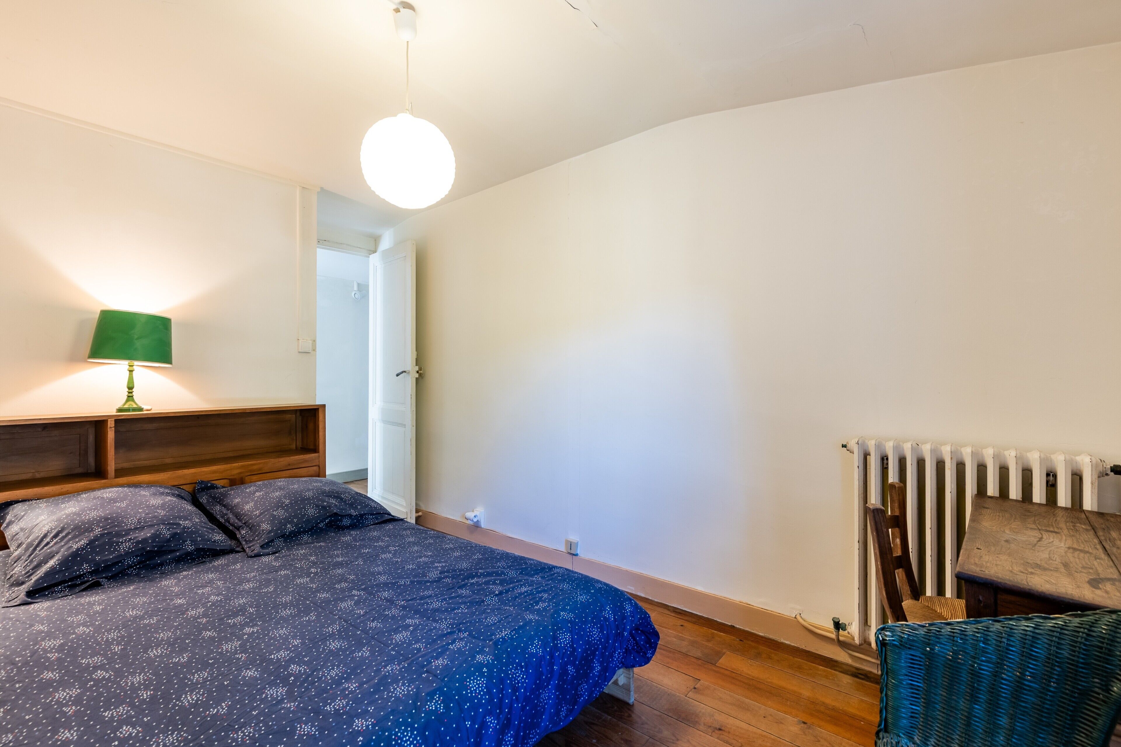 A bedroom with a bed, a green lamp, a radiator, and a wooden floor.