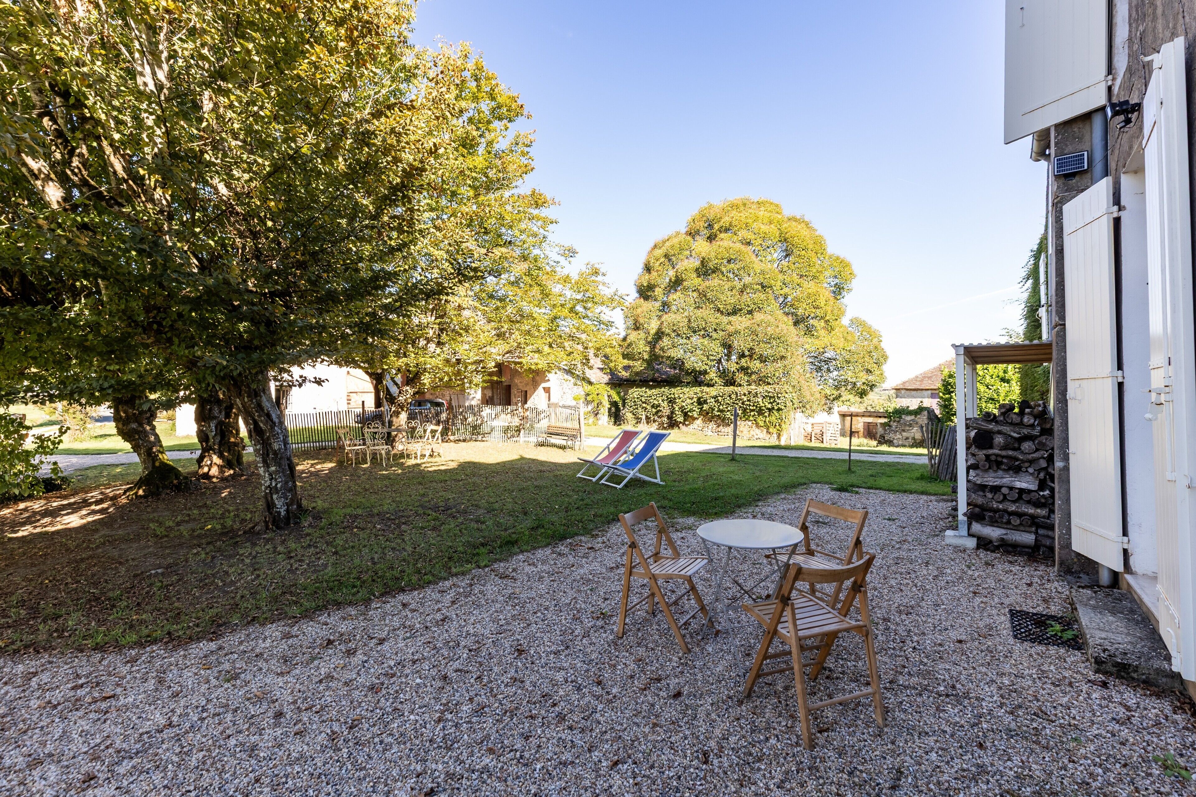 Une terrasse avec des sièges extérieurs, un arbre et un bâtiment à la façade blanche.