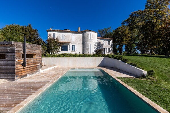 A large house with a swimming pool, surrounded by a well-maintained lawn and trees.