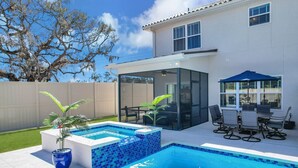 A backyard with a swimming pool, a covered patio, and a white house.