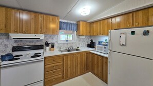 A kitchen with wooden cabinets, a white stove, a sink, a microwave, and a refrigerator. - Entire 3-bedroom 2-bath home that is only 2.5 miles from Sunset Beach ocean. (Sunset Beach)