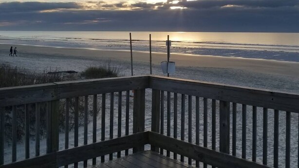 A wooden deck overlooking a beach with a sunset in the background. - Entire 3-bedroom 2-bath home that is only 2.5 miles from Sunset Beach ocean. (Sunset Beach)
