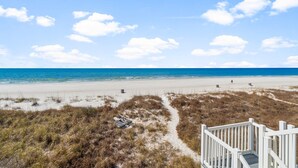 A beach with a white wooden walkway leading to a sandy area, a clear blue sky, and the ocean in the background. - Beachfront - West End PCB - Gulf Views (Panama City Beach)