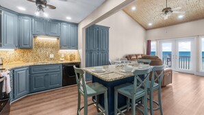 A kitchen with blue cabinets, a granite countertop, and a dining area with a table set for four. - Beachfront - West End PCB - Gulf Views (Panama City Beach)