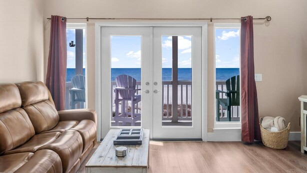 A living room with a brown leather sofa, a wooden coffee table, and a view of the beach through a glass door. - Beachfront - West End PCB - Gulf Views (Panama City Beach)