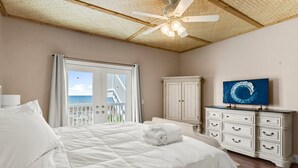 A bedroom with a bed, a dresser, a ceiling fan, a television, and a view of the ocean through a window. - Beachfront - West End PCB - Gulf Views (Panama City Beach)