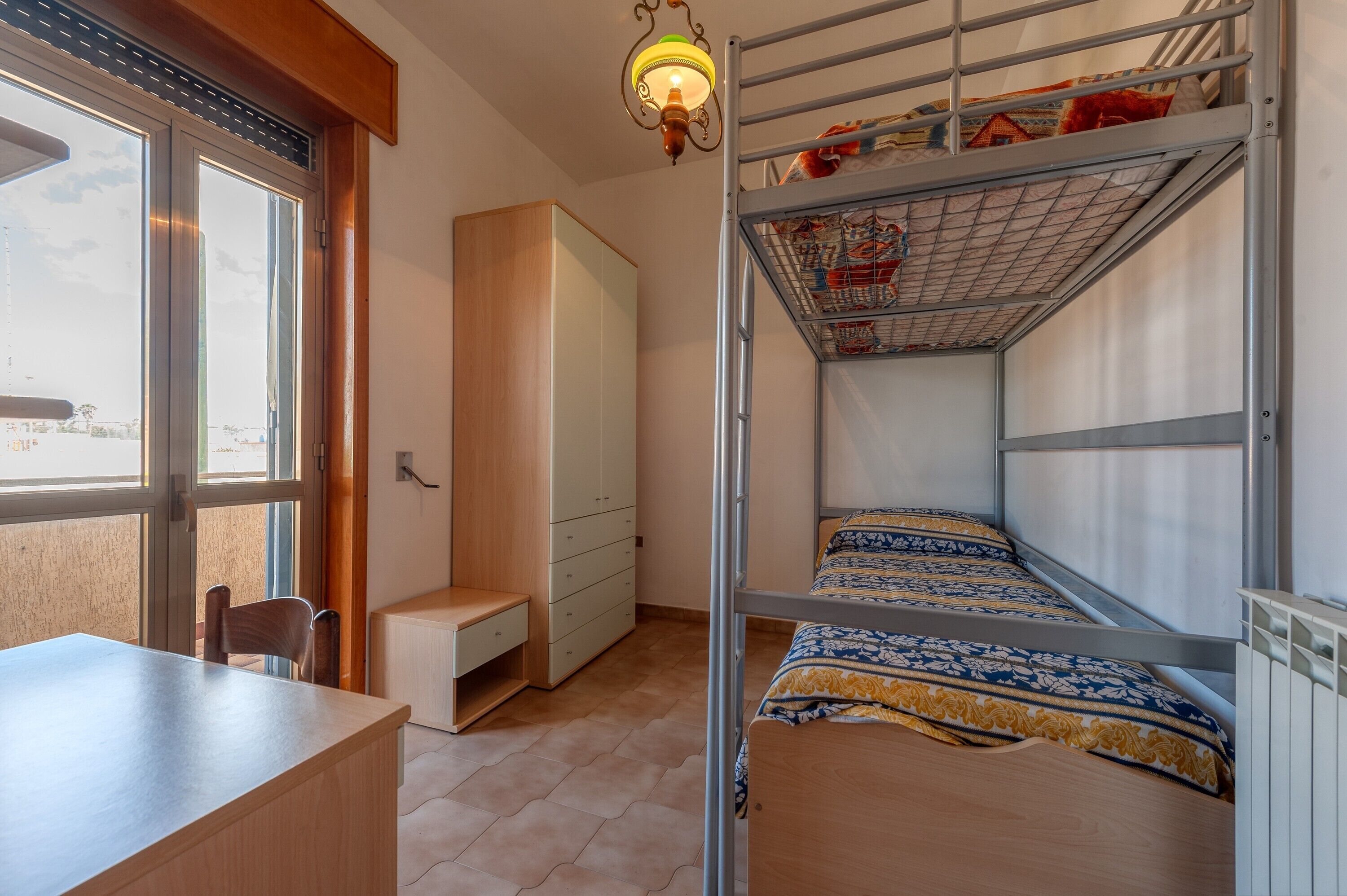 Un letto a castello con copripiumino decorato, una scrivania in legno, una sedia, un armadio e una finestra con vista.