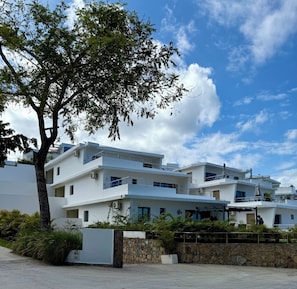 A modern multi-story building with white exterior walls, balconies, and air conditioning units.